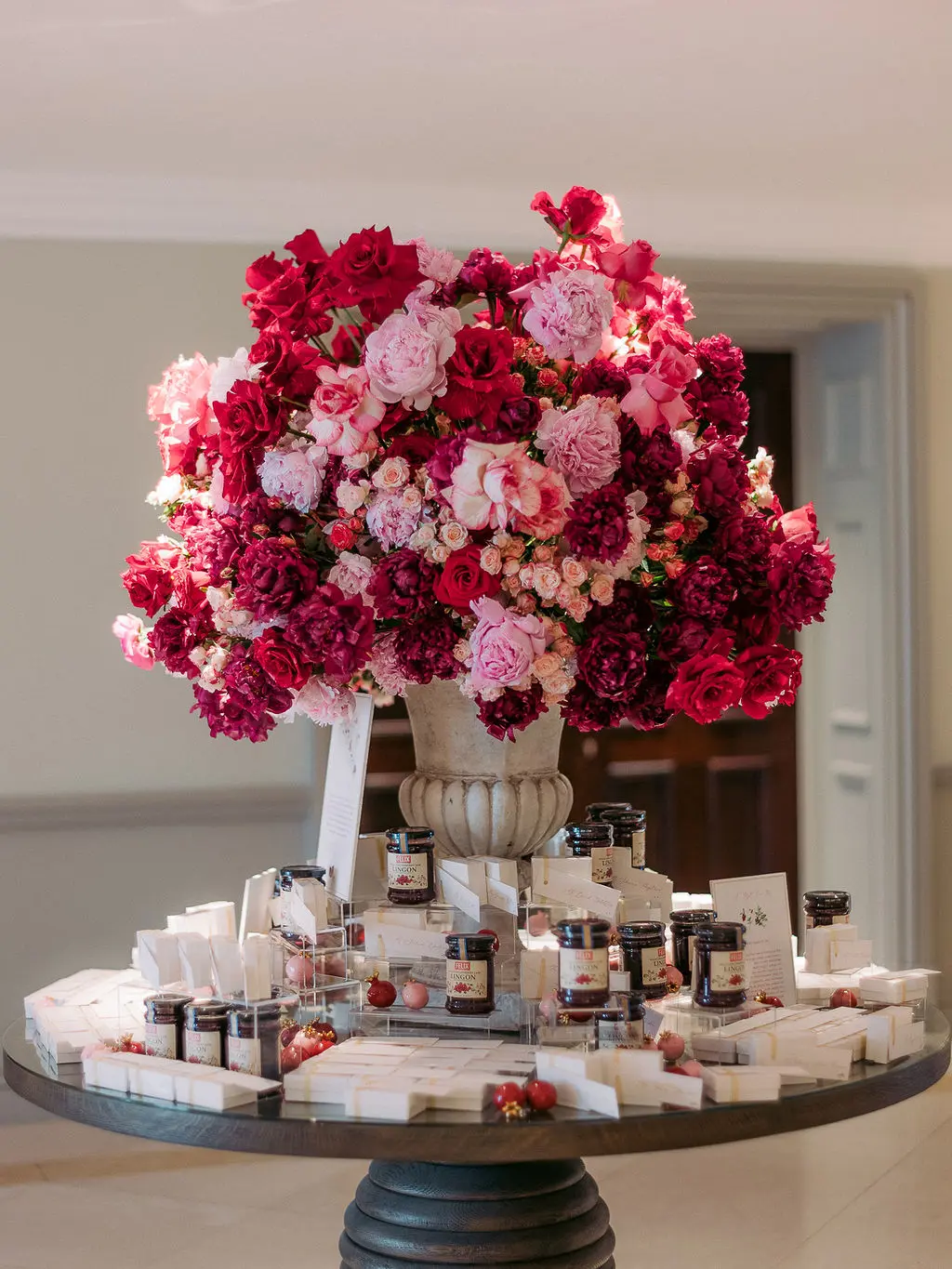 Large display of pink and red roses in centre of table surrounded by Swedish Jam and bespoke porcelain pomegranates