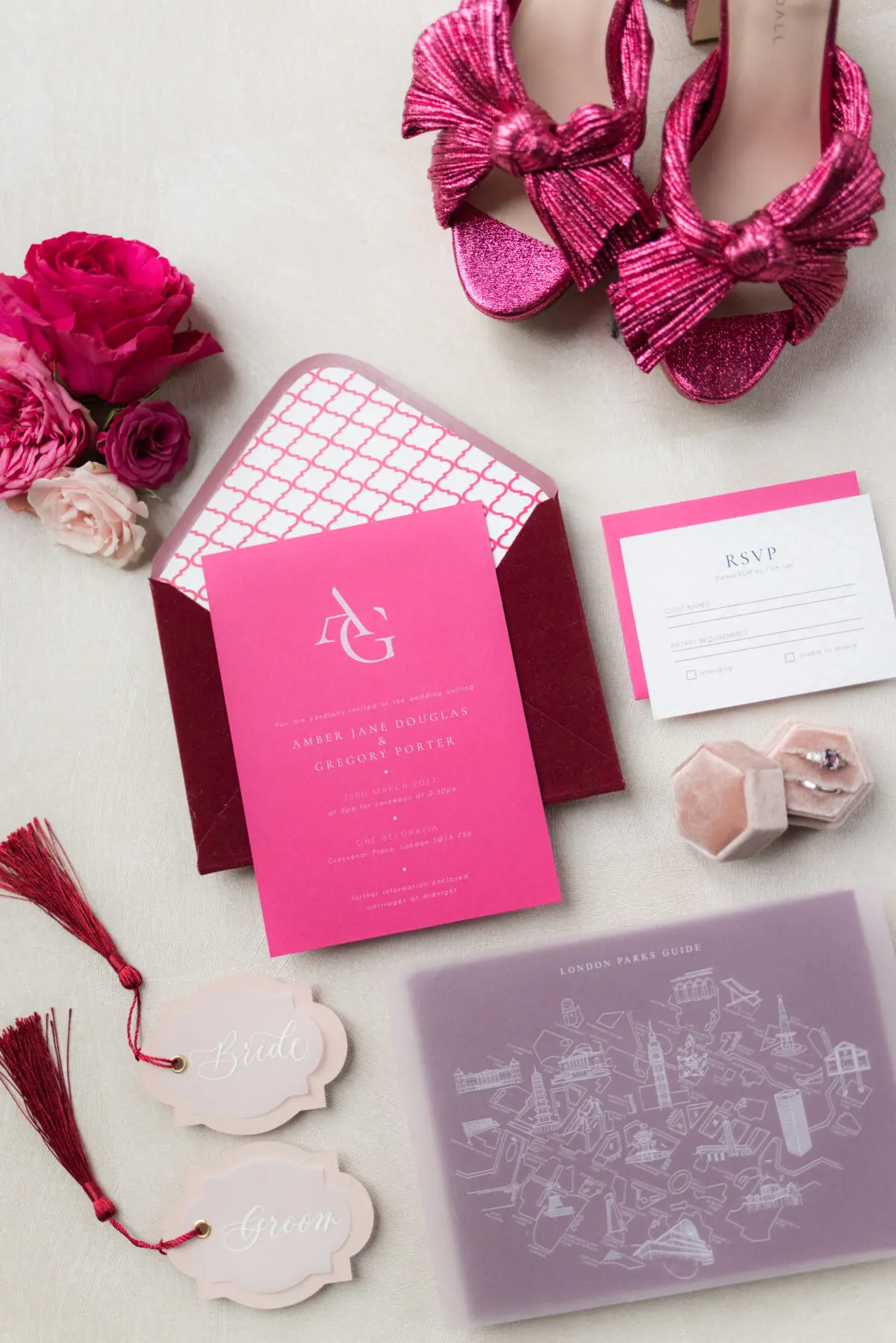 Flat lay of magenta and dark red coloured invitation suite with engagement ring in box and pink shoes