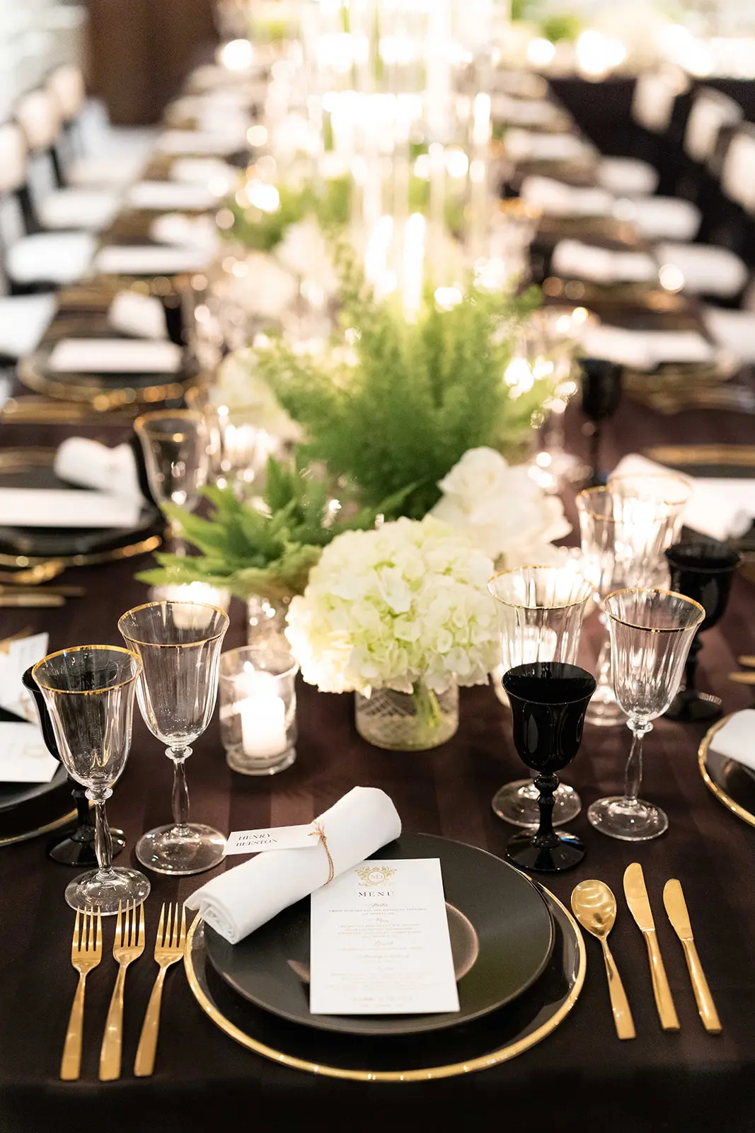 close up image of table design, gold cutlery on black table cloth with white and green flowers - monochrome wedding