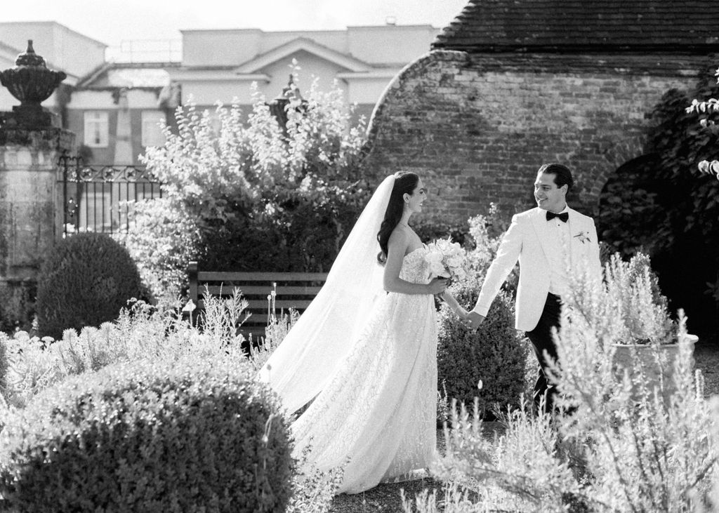 Black and white image of bride and groom walking through the gardens at Four Seasons Hampshire