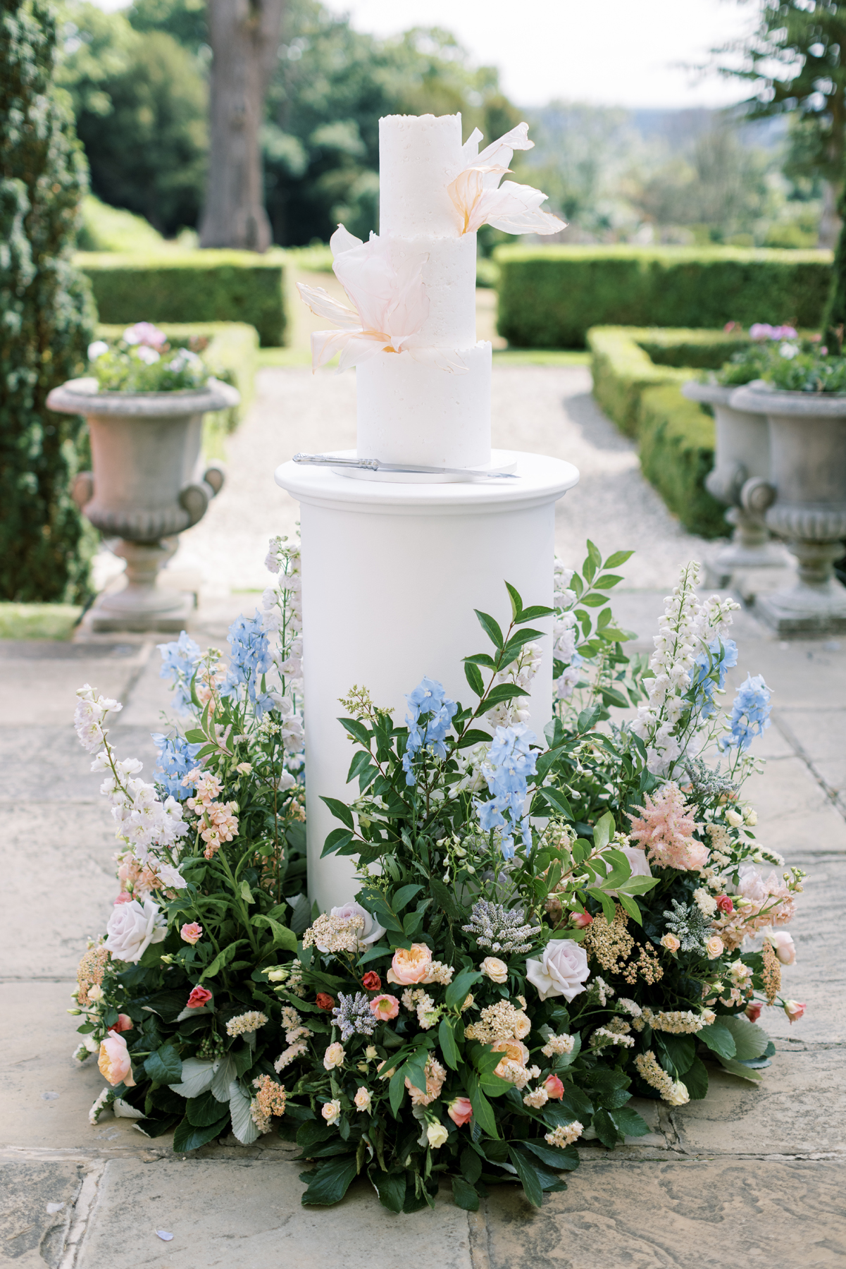 Hedsor House wedding Planner - three tier wedding cake sitting on white plinth surrounded in flowers